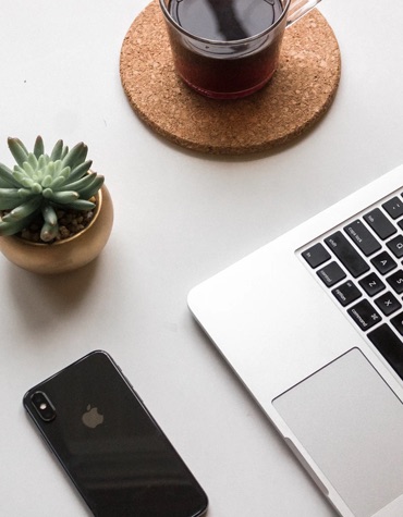 View of a macbook laptop, iPhone, cactus plant, and a cup of coffee on a desk.